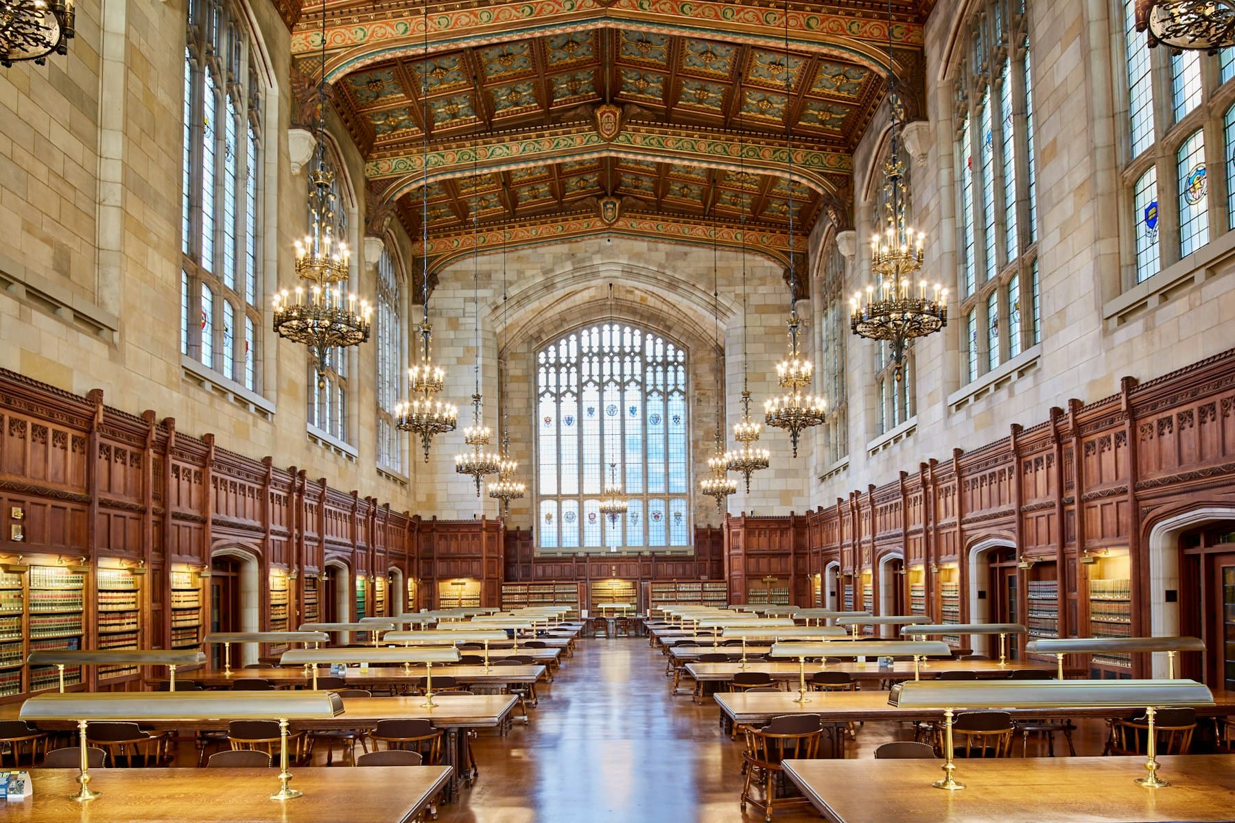 A grand university reading room with long desks and chandeliers